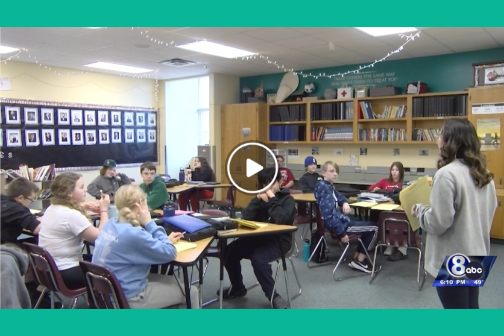 Still from Channel 8 news video with classroom full of students and teacher in the front.