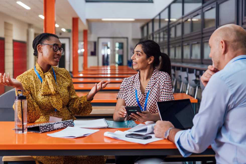 Three teachers talk at a table.