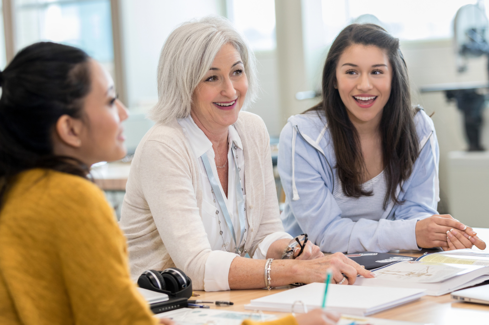 Three teachers smiling while working together at a table.